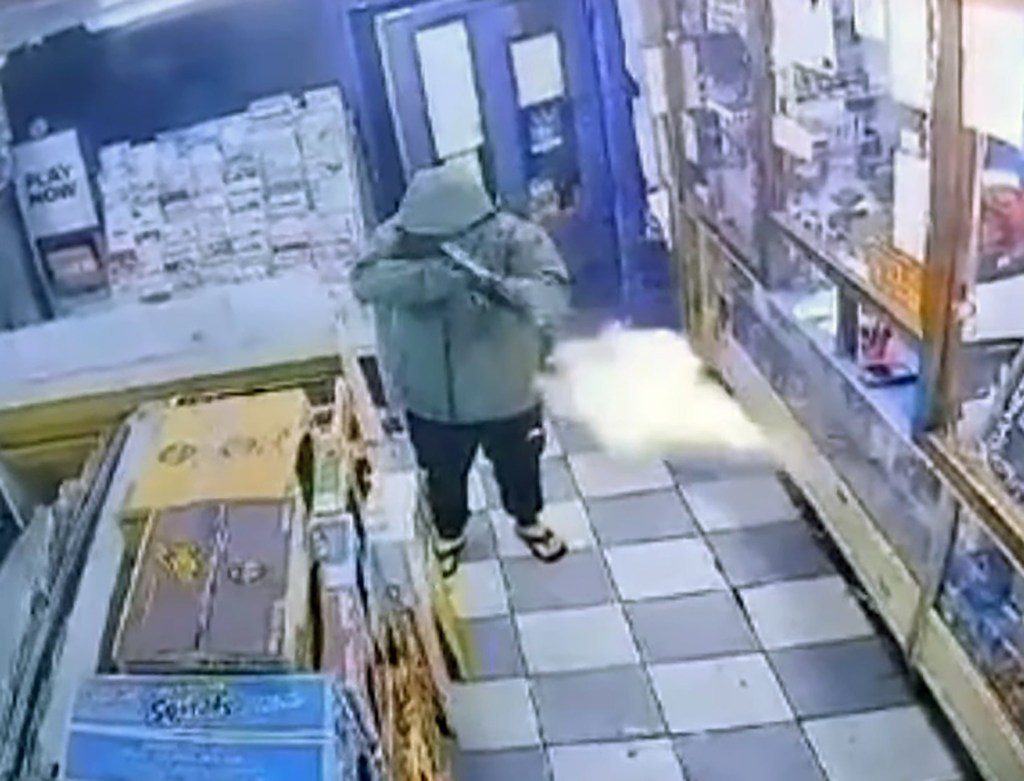 Leslie Garrett in a coat with his hood up as he fires a gun into the perspex screen of a newsagents.