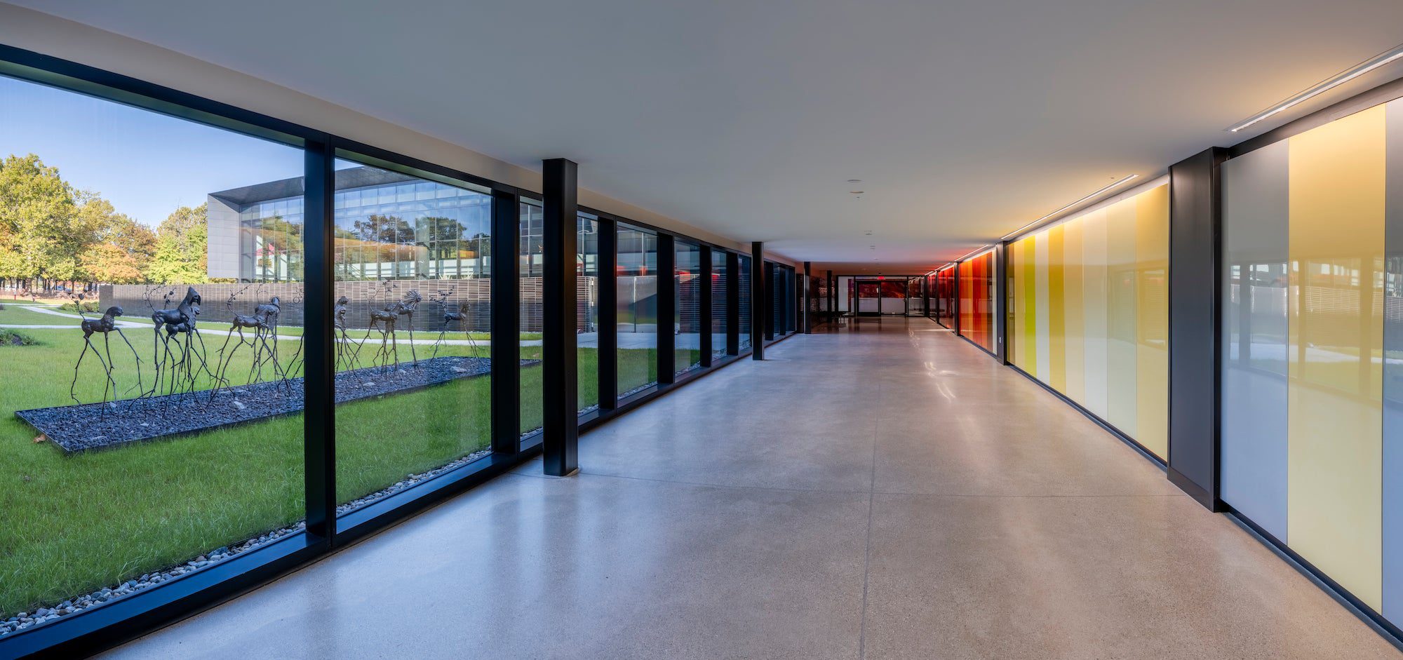 a hallway with large windows on one side and shades of yellow and blue on the other wall