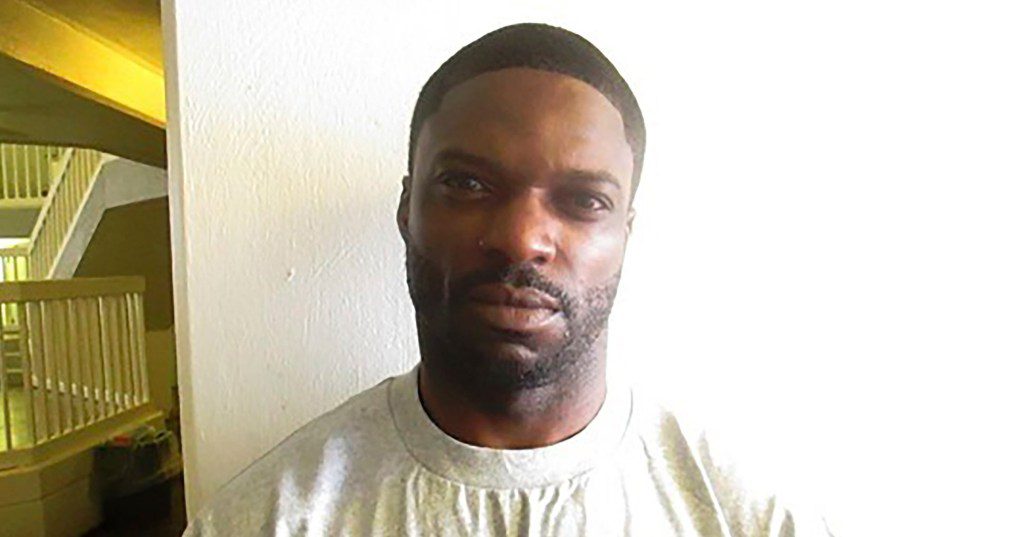 Michael Dewayne Smith looks into the camera while standing in front of a white wall.