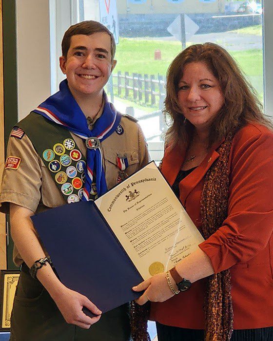 Boy Scout in uniform receiving proclamation from female state representative.